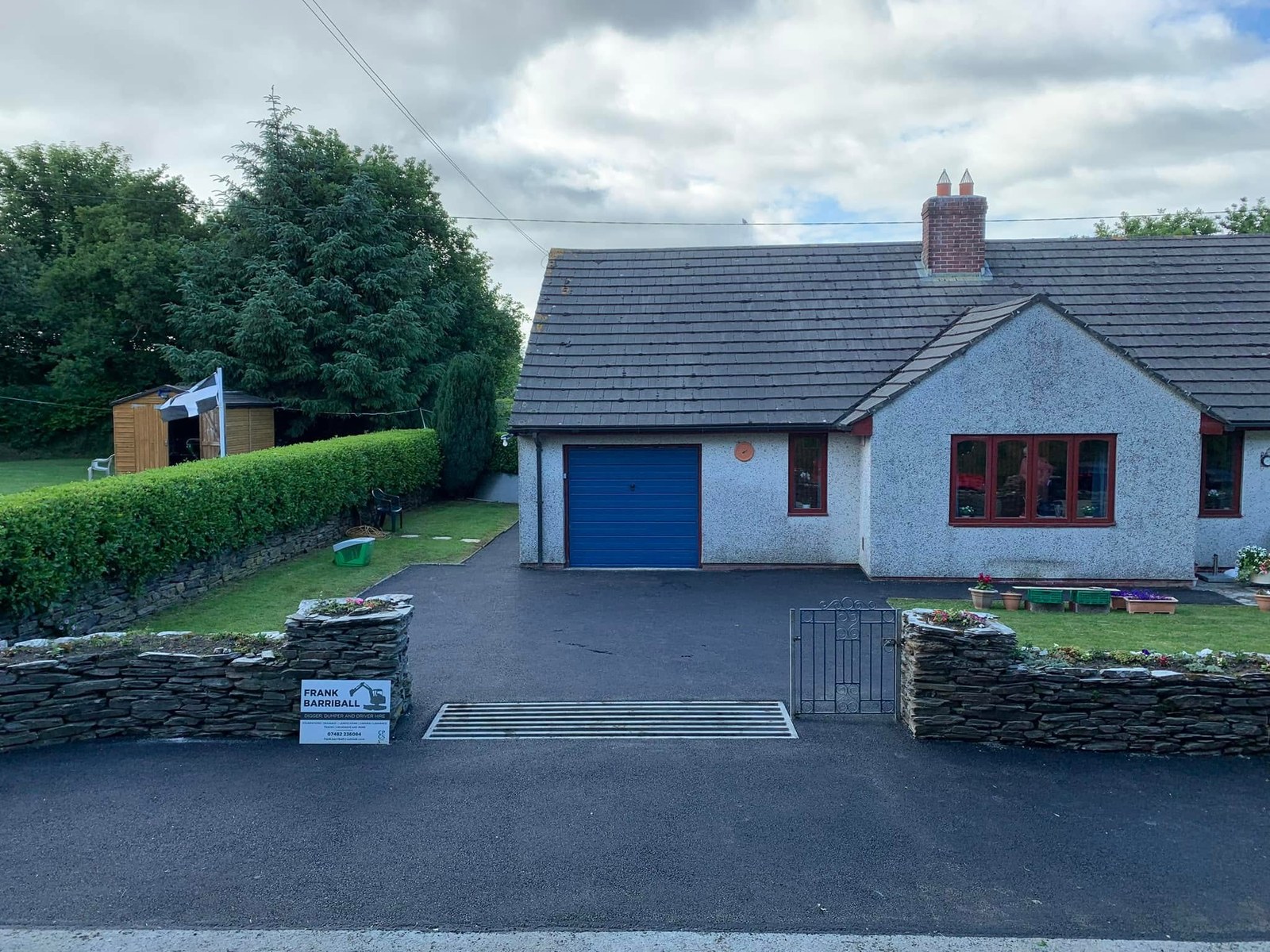 Finished dark driveway leading to a bungalow with a blue garage door