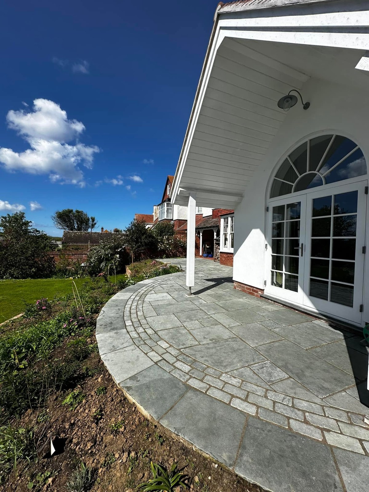 Curved paved patio wrapping around the front of a white house